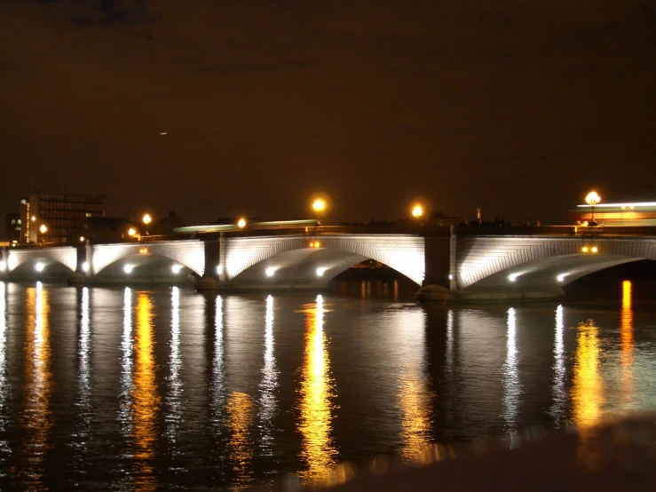 a bridge is shining brightly at night and reflecting water