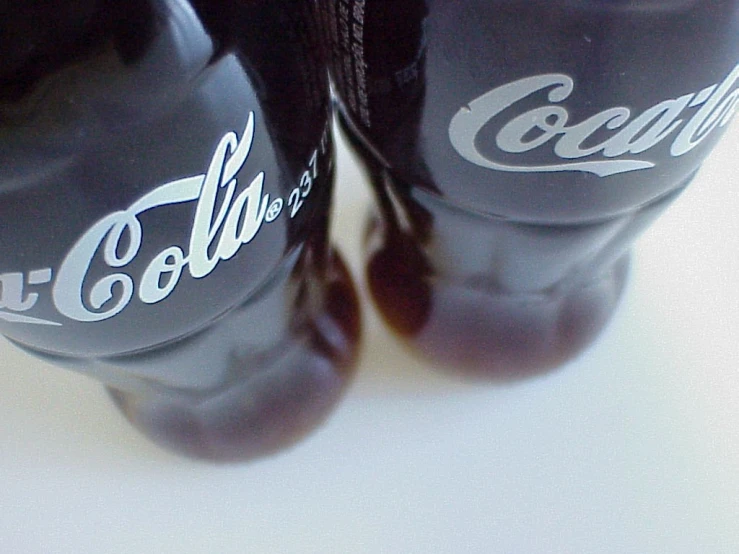 two black cola bottles are next to each other