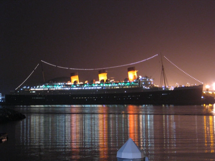 the cruise ship is moored at night and the reflection in the water is just across the fence