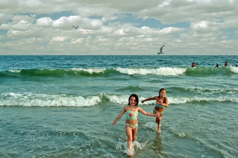 two young ladies run through the ocean water