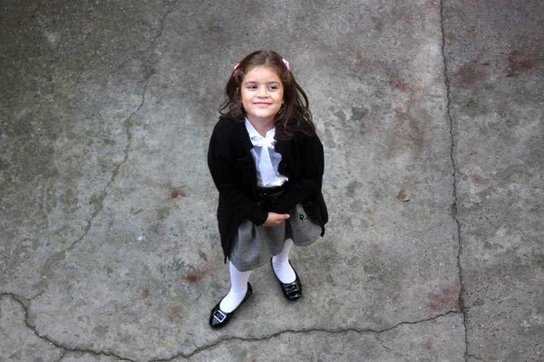 a girl smiling at the camera while sitting on concrete