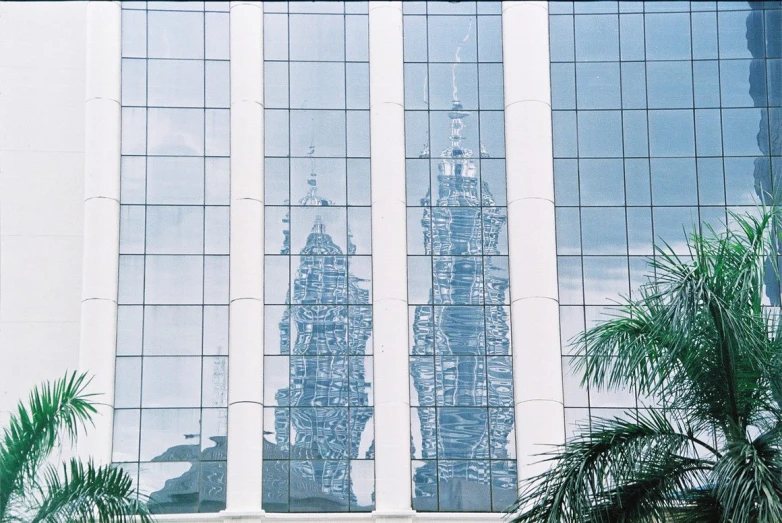 a building reflecting in a mirror with trees and a sky background