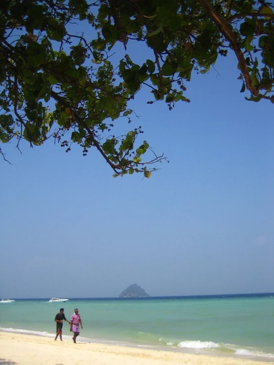 two people walking on a beach with clear blue waters