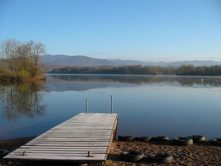 a dock on the shore of a lake with water and some trees