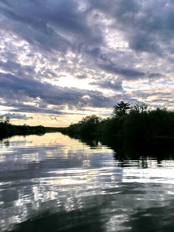 a body of water with trees and clouds above it