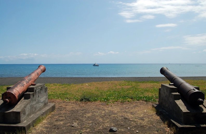 two old cannon's sitting side by side on concrete bases overlooking the beach