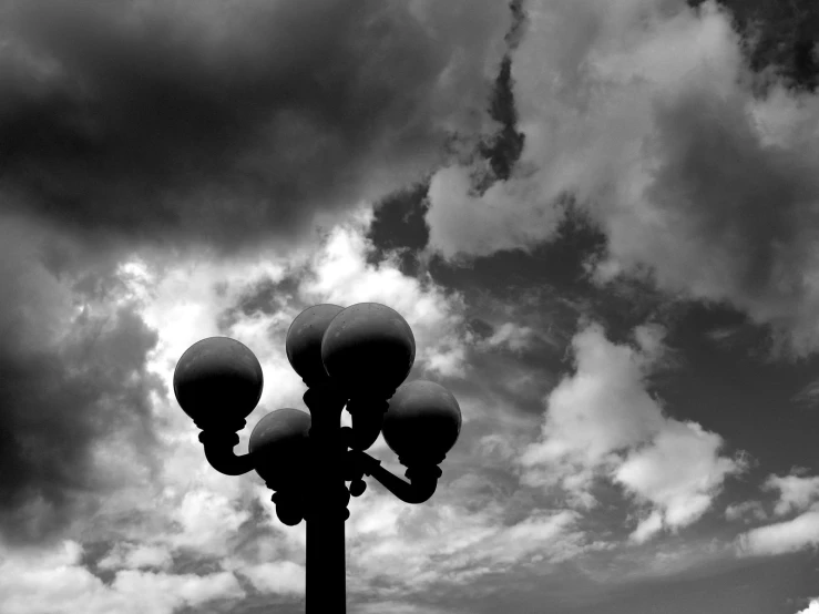 black and white image of street lights against the cloudy sky