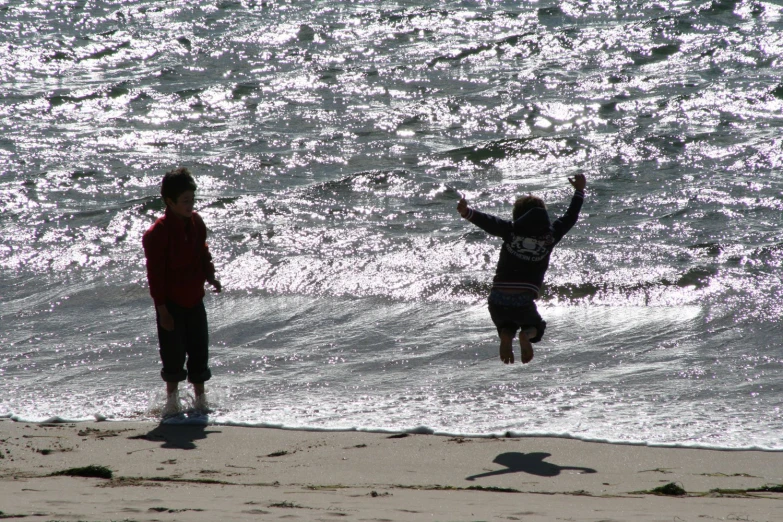two people jumping up in the air above water on a beach