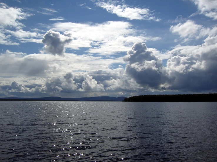 a lake with a forest on the far side and clouds in the air