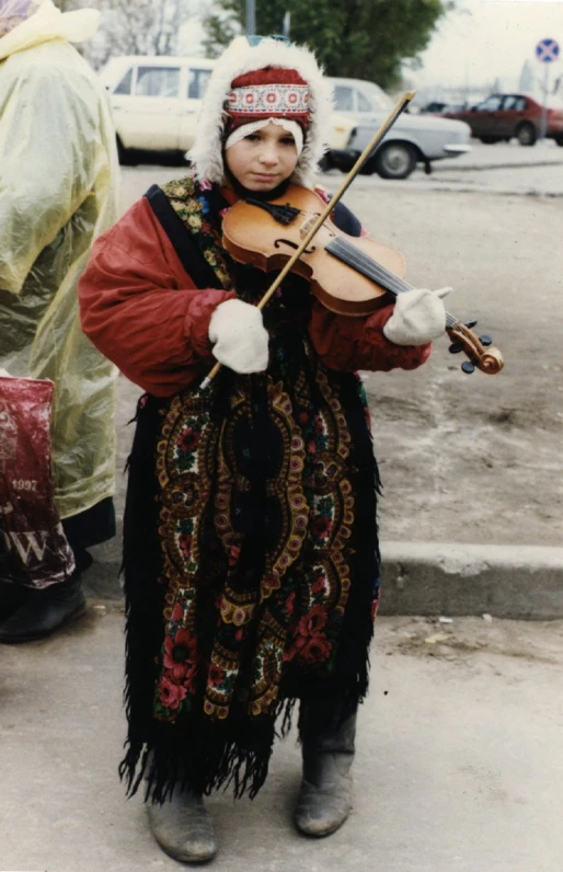 a young man dressed in folk clothes holds a violin in one hand