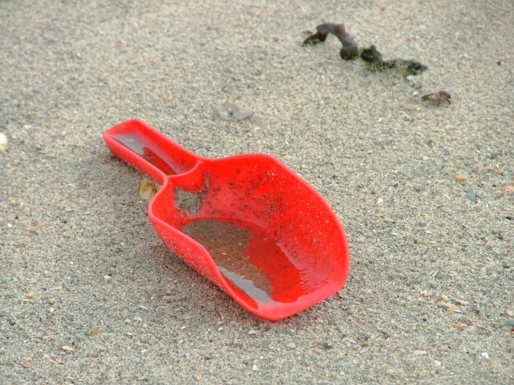 a red shovel lying on top of a sandy beach
