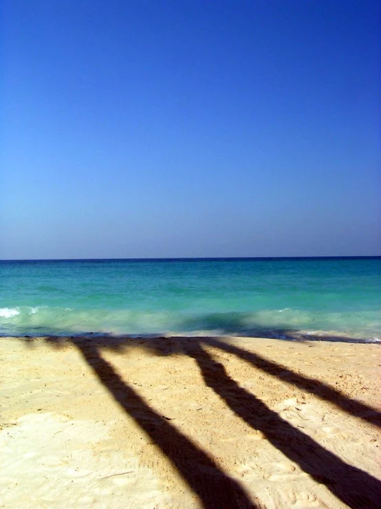 the shadow of two people standing at the edge of the water