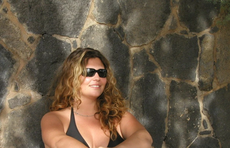 a woman poses against a rock wall with her arm wrapped