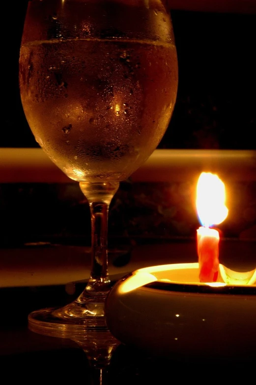 a lit candle on a cake sits next to a glass