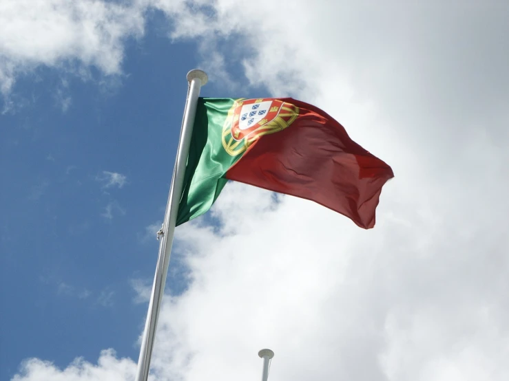 an portugal flag is flying in the wind with blue cloudy sky behind