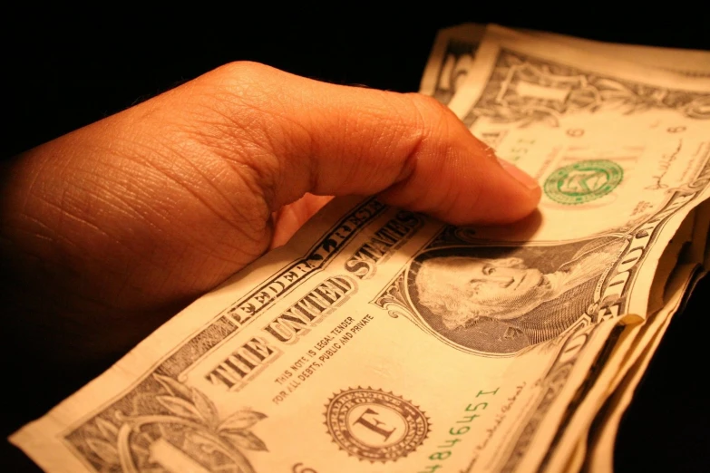 a person is holding out a knife on top of a stack of one dollar bills