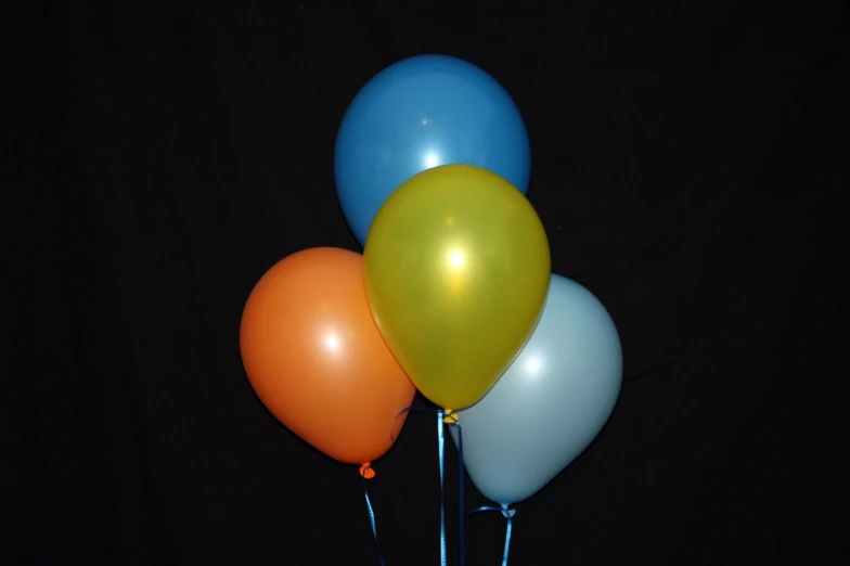 four colorful balloons in a clear vase with black background