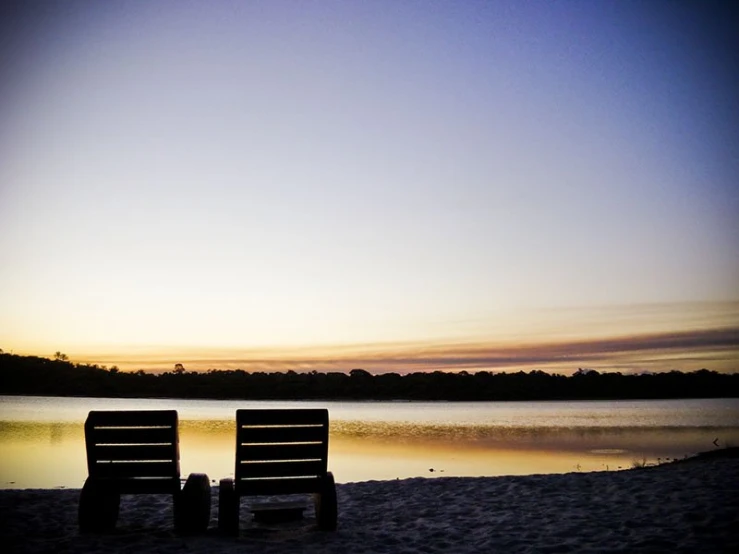 two empty benches are near the water at sunset