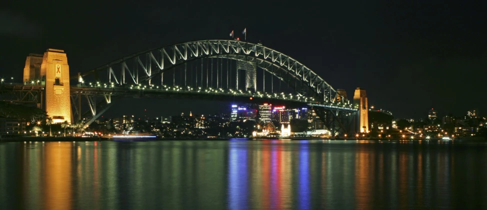 the sydney skyline illuminated up at night with a large bridge in the distance