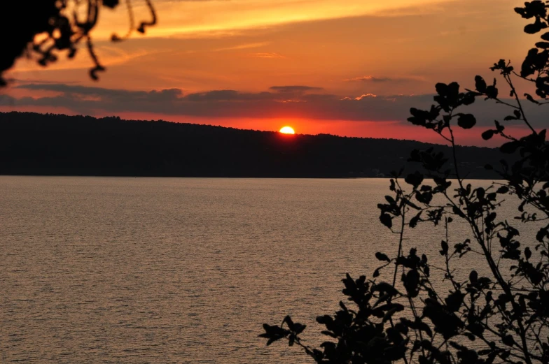 a sunset seen over some water with trees in the foreground