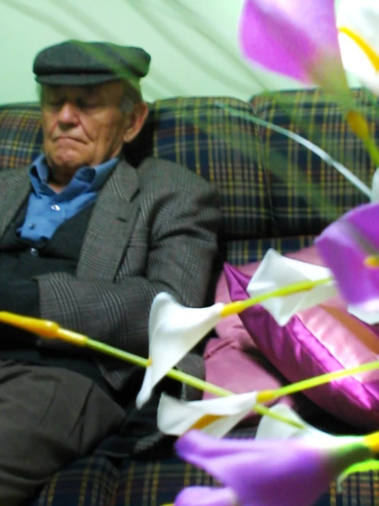 an old man sitting on a couch with many flower petals