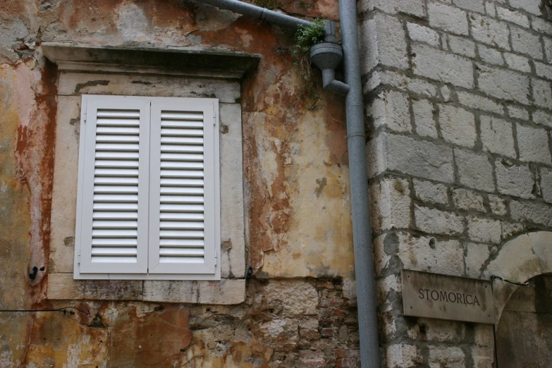 a stone wall with white shutters next to an urban building