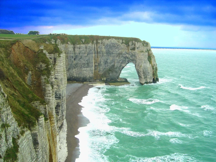 a large long cliff near the ocean with a beach and grassy hillside