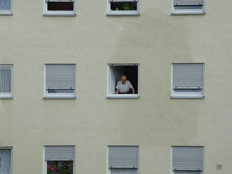 man with white shirt looking out windows, while holding cell phone