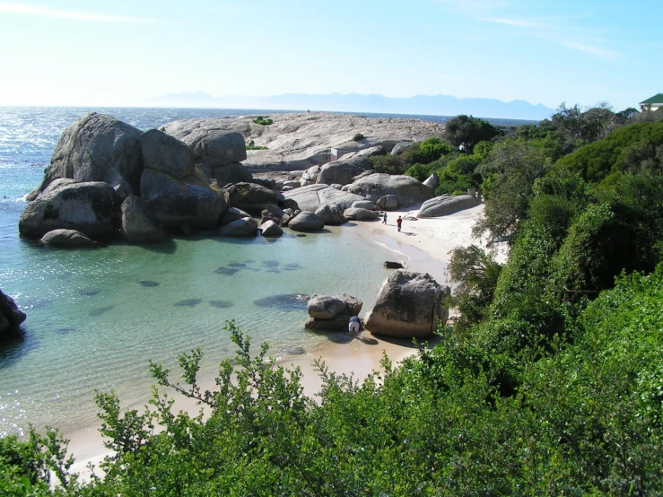 people enjoy the sand beach with boulders on a sunny day