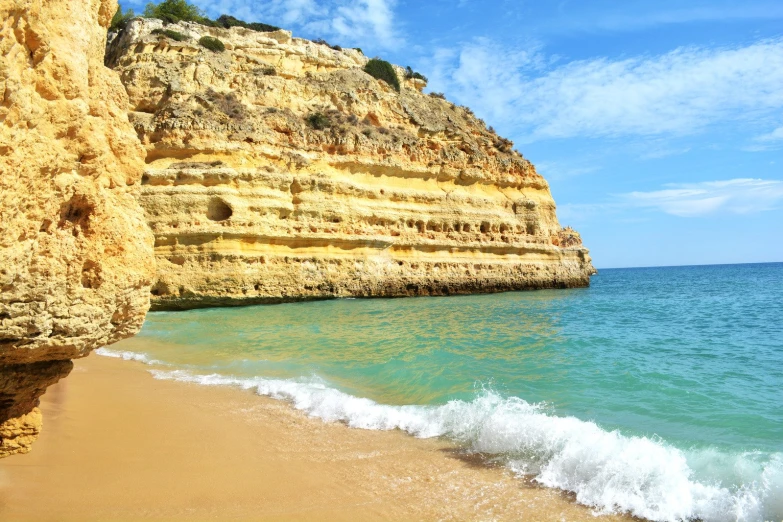 waves and waves hitting the beach next to a cliff