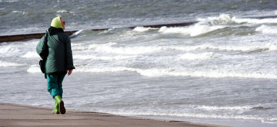 a person walks along the ocean water holding a backpack