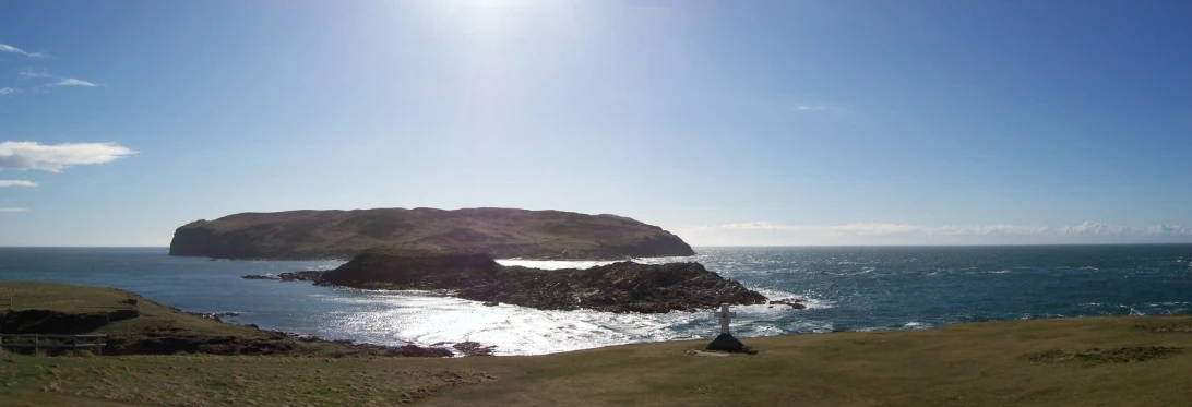 the sun shines on a large rock on a grassy hill