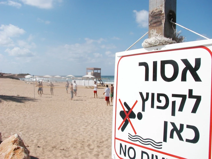 a sign in black and red on the sand of a beach