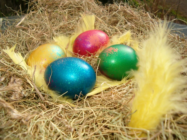 three brightly colored eggs laying on top of hay