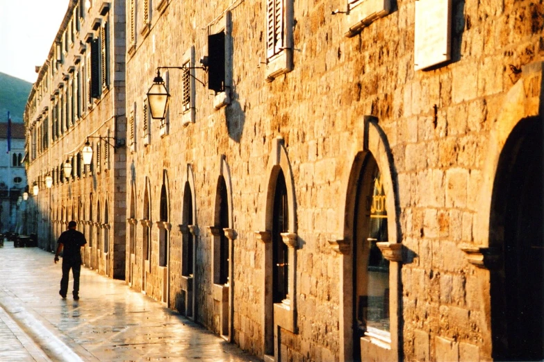 a man with an umbrella walks along a cobbled street