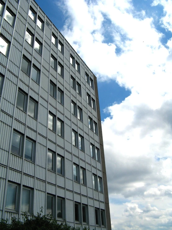 a tall grey building under blue skies with a tree