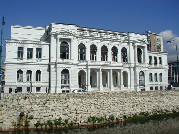 large white house with white trim on corner by a stone wall