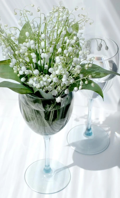 two wine glasses with vases containing flowers in them