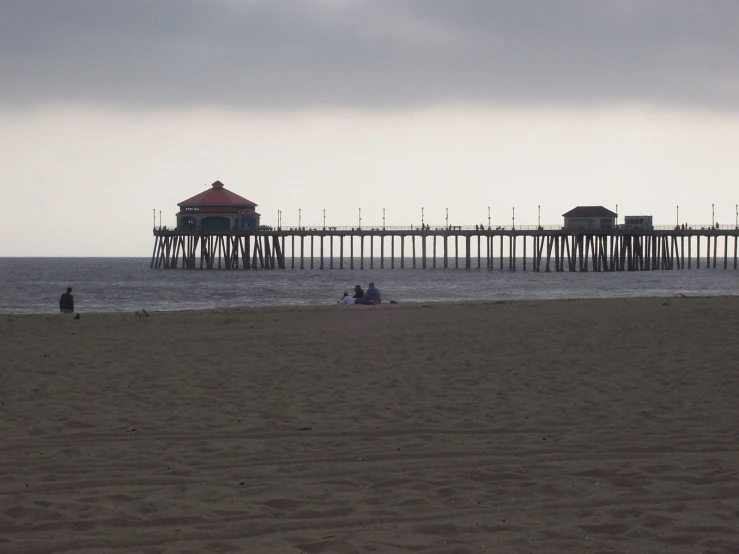 a person sitting in the sand near the beach next to a pier