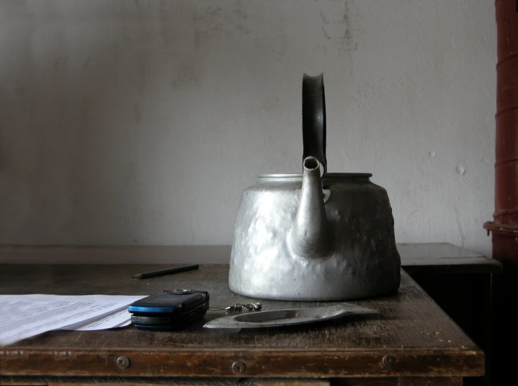 a silver teapot on a wooden table with paper and scissors