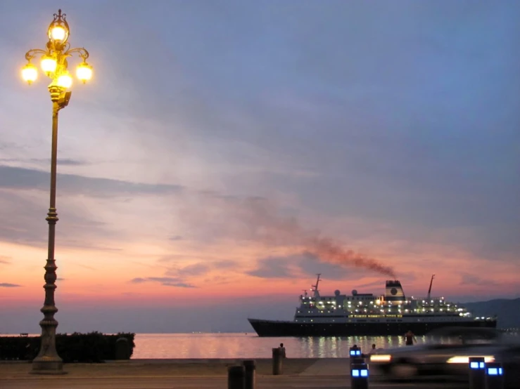 a cruise ship going by a street lamp with cars passing