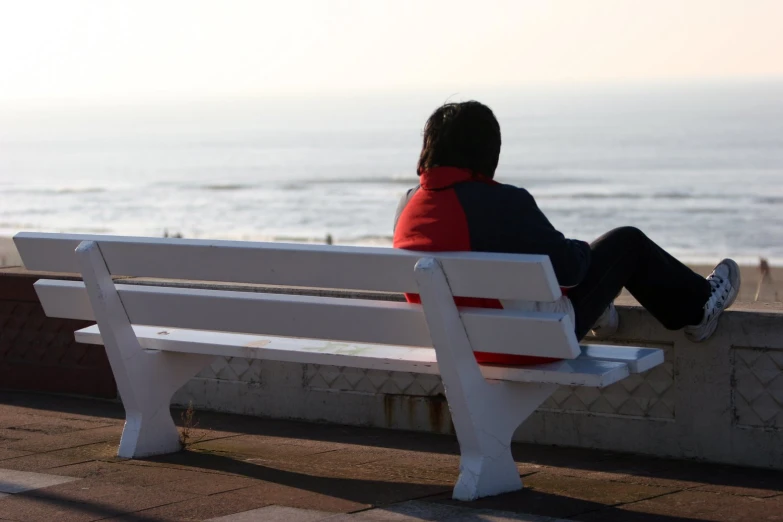 a person is sitting on a white bench overlooking the ocean