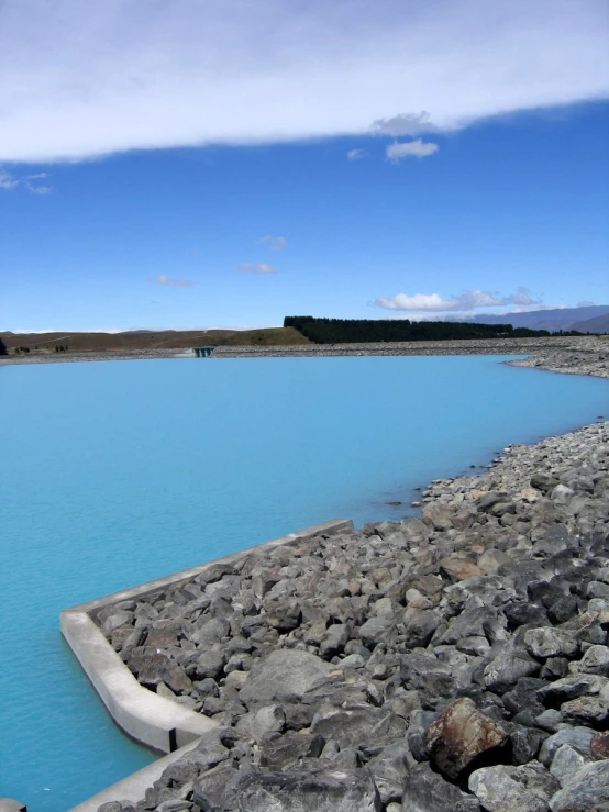 a view of a blue pond next to a rocky shoreline