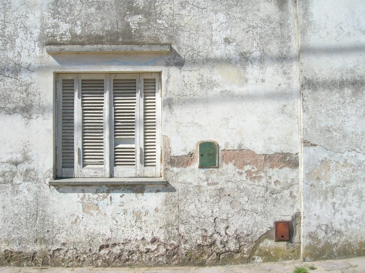 a building with a window with shutters and a rusted stop sign