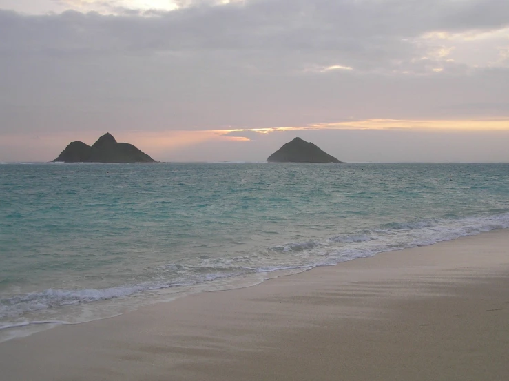 an empty beach during the day with two island in the background