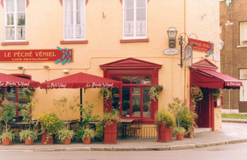 a corner cafe with red and white awnings, potted plants, and flower boxes