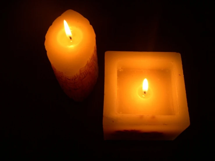 two candle lit on dark background, one on the other