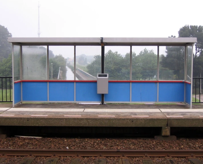 a blue and red bus stop with a clock near by