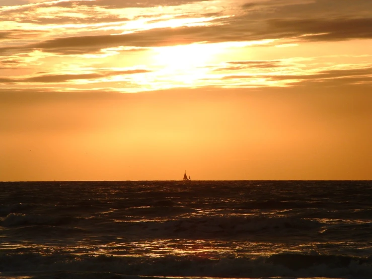 the sun is setting over an ocean with a sailboat