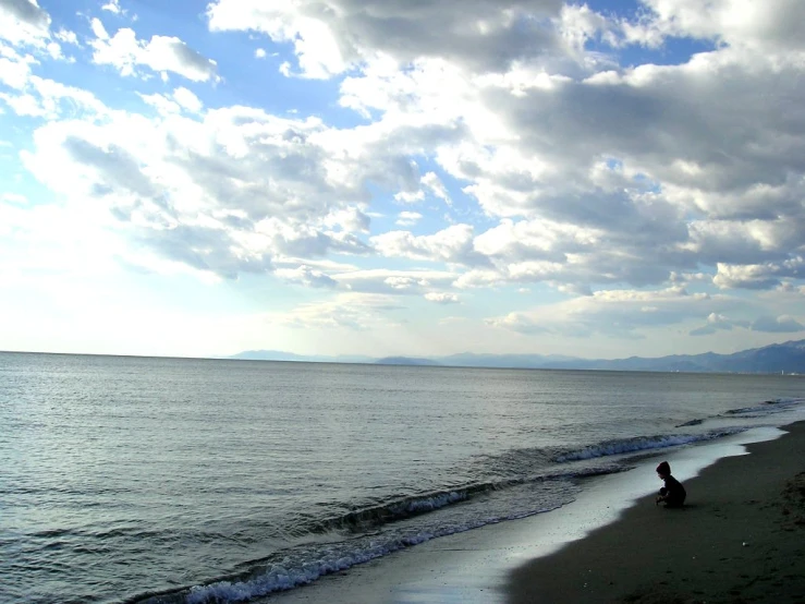 person sitting on shore watching the ocean from a beach